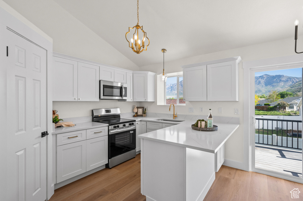 Kitchen with stainless steel appliances, a sink, a peninsula, lofted ceiling, and white cabinetry