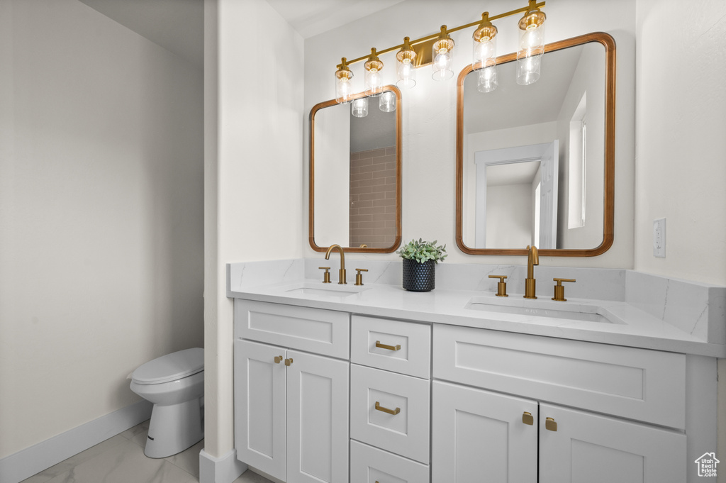Bathroom with marble finish floors, baseboards, toilet, and double vanity