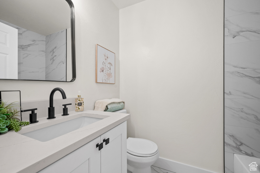 Bathroom featuring marble look tiles, toilet, vanity, and baseboards