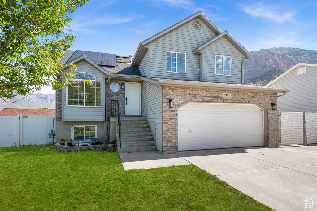 View of front of house featuring concrete driveway, solar panels, a garage, brick siding, and a mountain view
