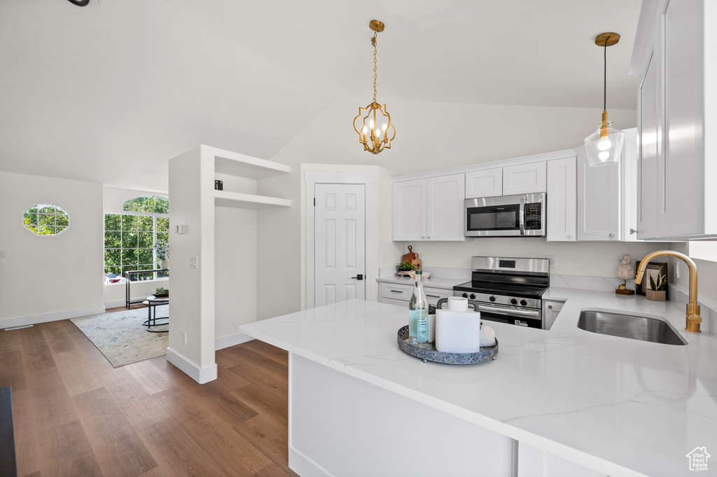 Kitchen with appliances with stainless steel finishes, a sink, white cabinets, a peninsula, and light stone counters