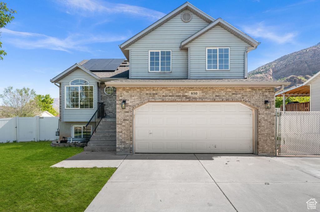 View of front facade featuring a gate, solar panels, brick siding, and driveway