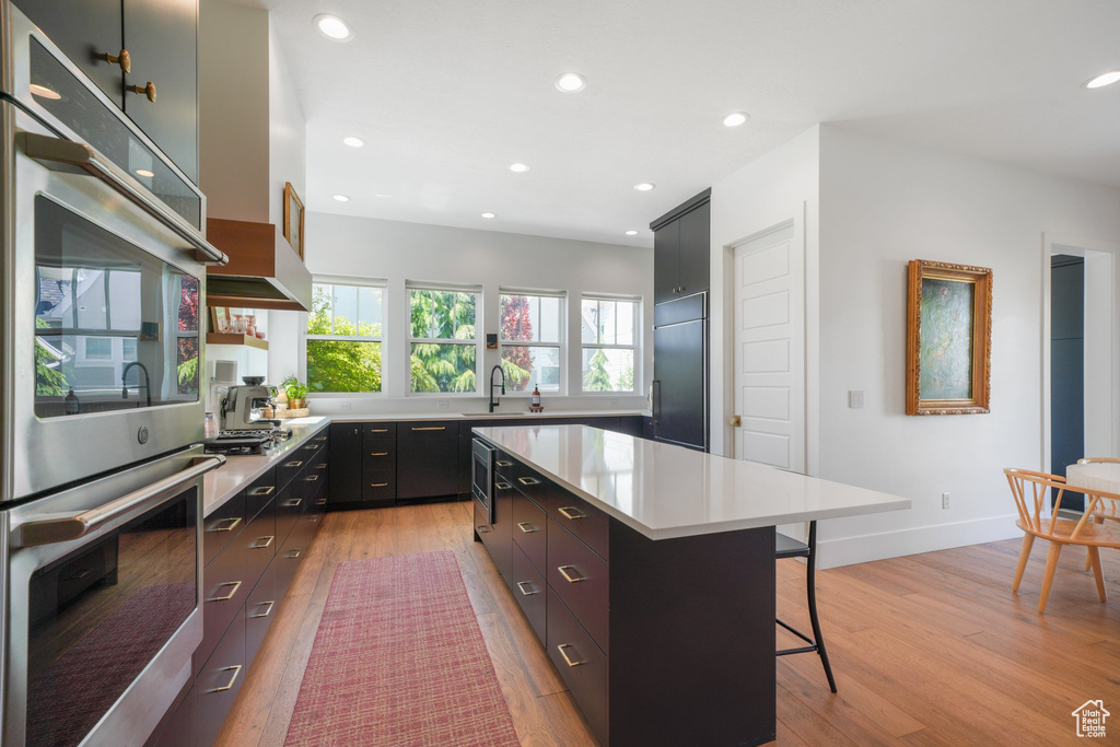 Kitchen featuring stainless steel appliances, a breakfast bar, light wood-style floors, light countertops, and recessed lighting