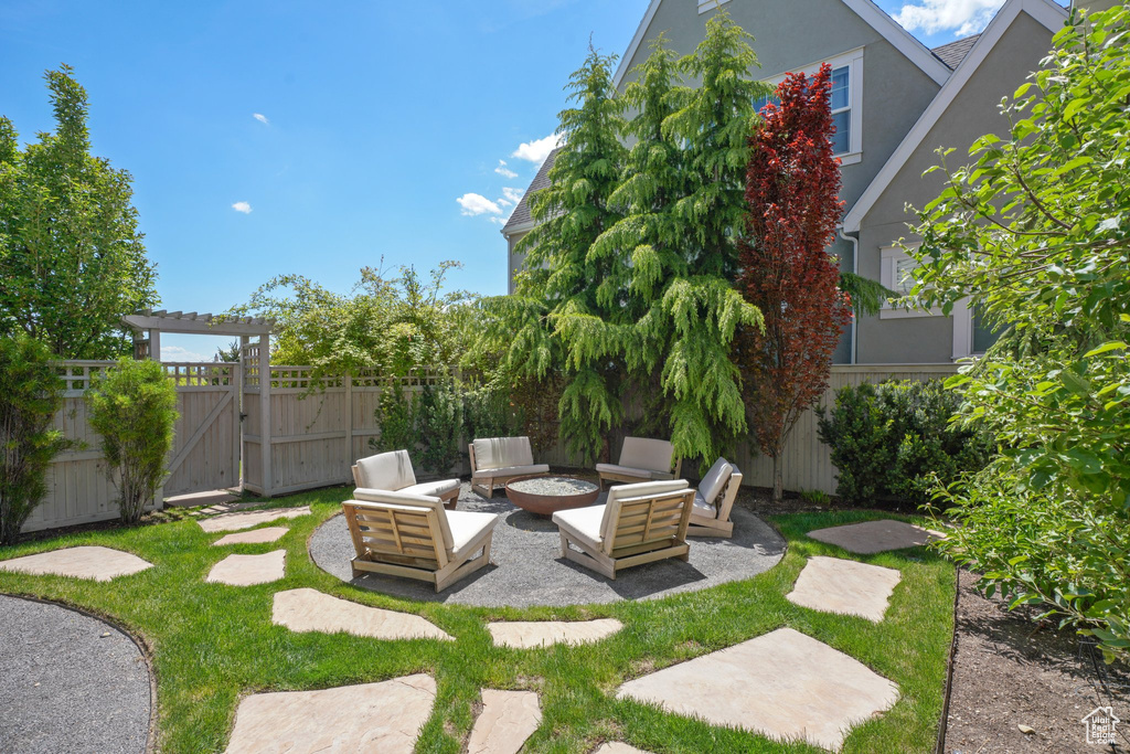 View of yard featuring fence, a gate, an outdoor living space with a fire pit, and a patio
