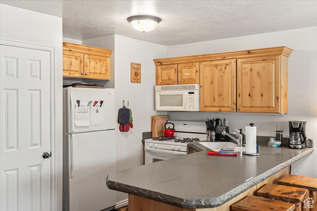 Kitchen featuring a breakfast bar, white appliances, a sink, a peninsula, and dark countertops