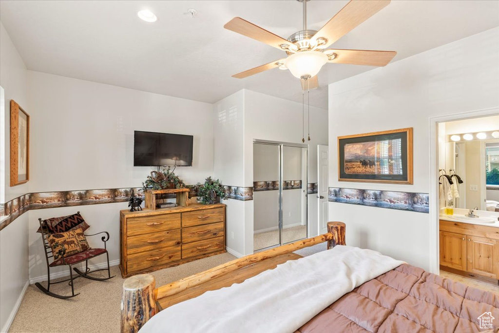 Carpeted bedroom featuring a closet, baseboards, ensuite bath, ceiling fan, and a sink