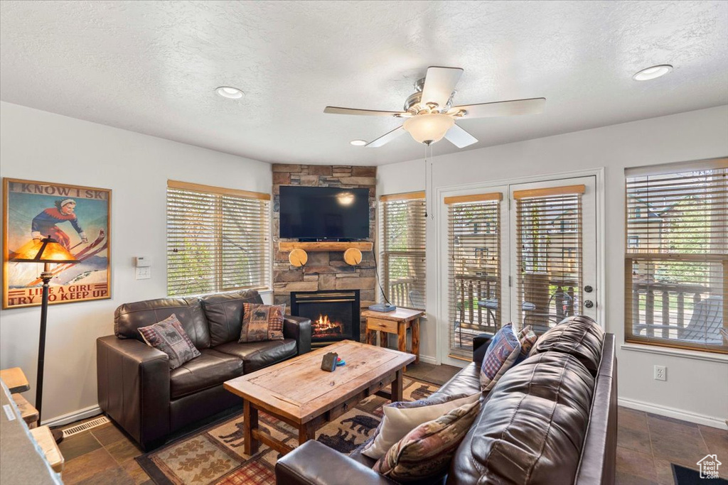 Living room with a textured ceiling, baseboards, a stone fireplace, and a ceiling fan