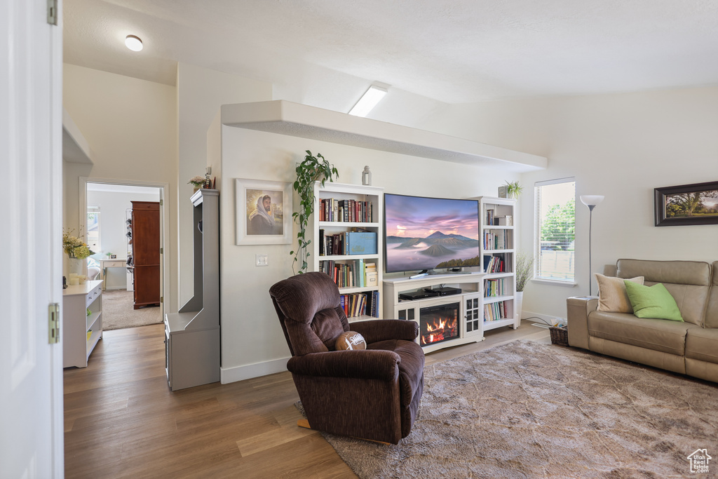 Living area featuring wood finished floors, a glass covered fireplace, lofted ceiling, and baseboards
