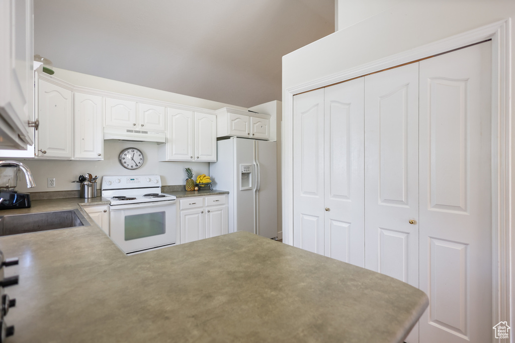 Kitchen featuring white appliances, a sink, under cabinet range hood, white cabinetry, and a peninsula