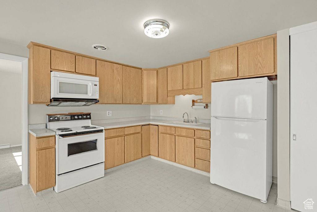 Kitchen with white appliances, a sink, light countertops, light brown cabinetry, and light flooring