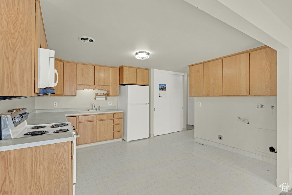 Kitchen with white appliances, light countertops, light brown cabinets, and a sink