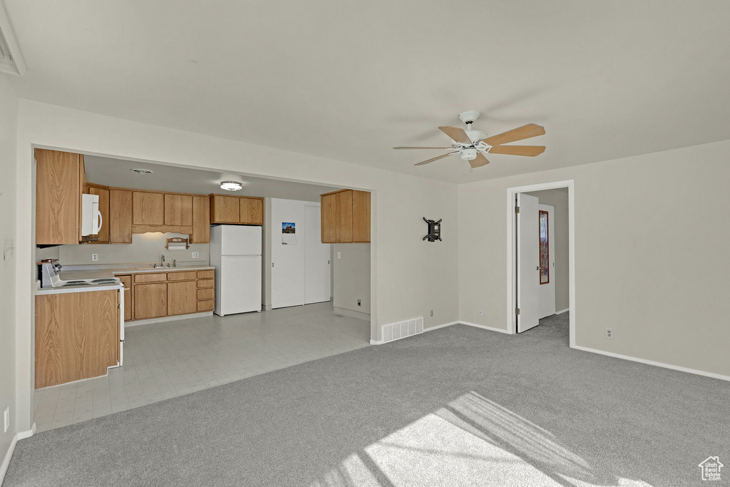 Unfurnished living room featuring a sink, ceiling fan, baseboards, and light colored carpet