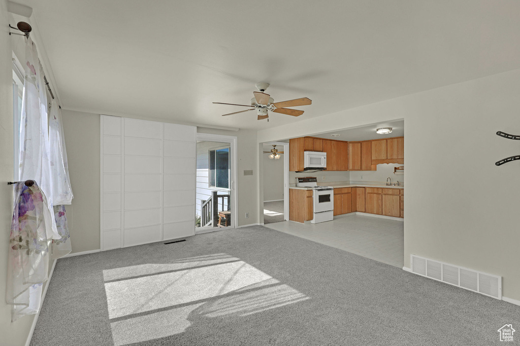 Unfurnished living room with a ceiling fan, light carpet, and healthy amount of natural light