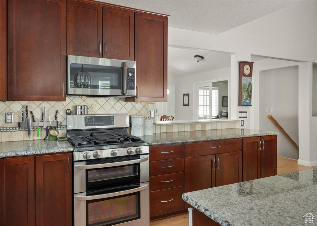 Kitchen with appliances with stainless steel finishes, light wood-style floors, backsplash, and light stone countertops
