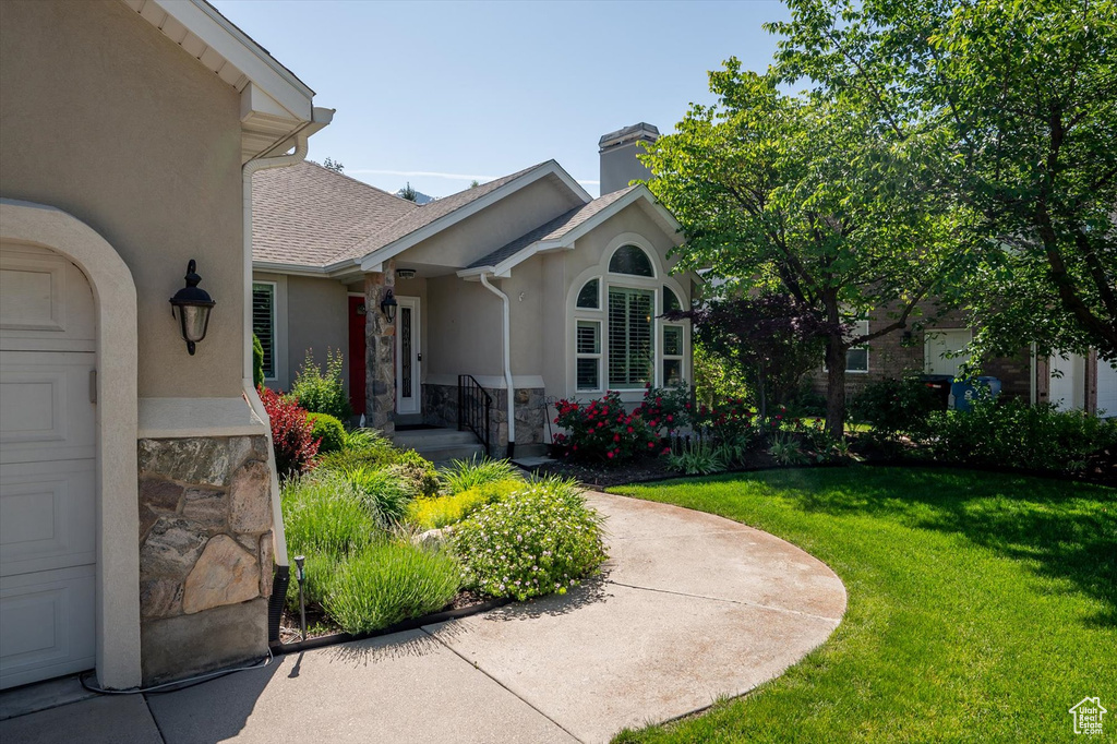 View of exterior entry with stucco siding, a yard, a chimney, stone siding, and roof with shingles