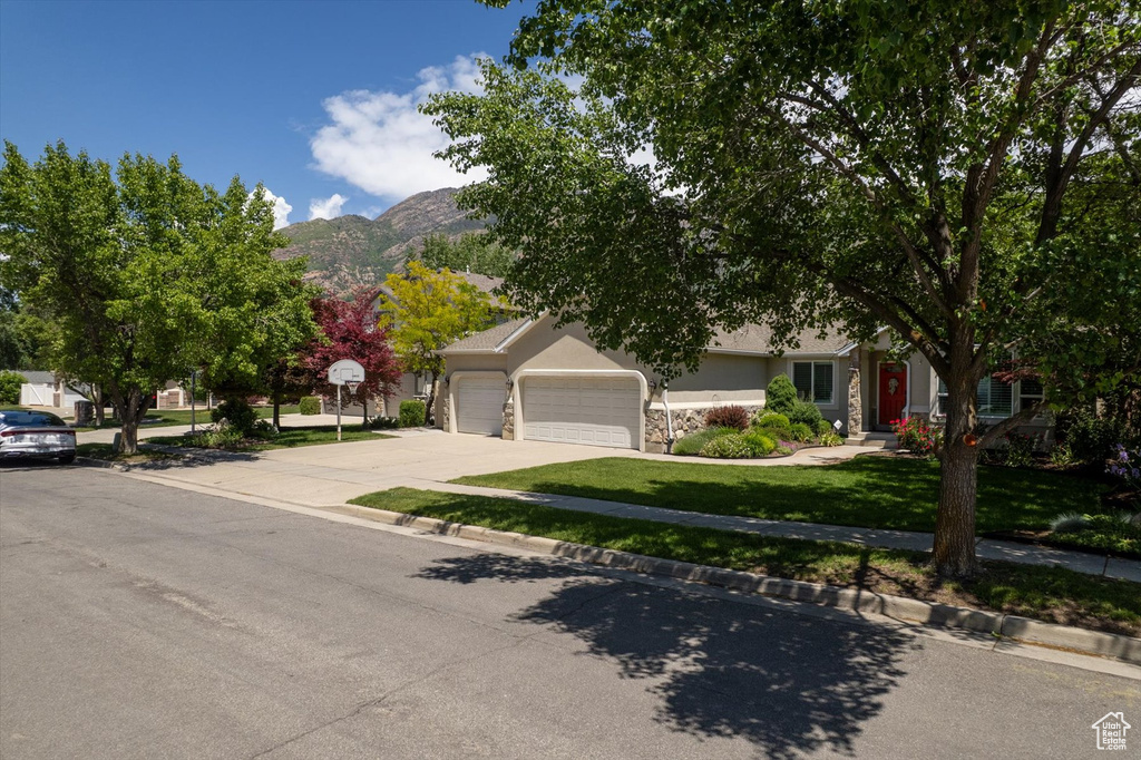 Obstructed view of property featuring a garage, a mountain view, driveway, a front yard, and stucco siding