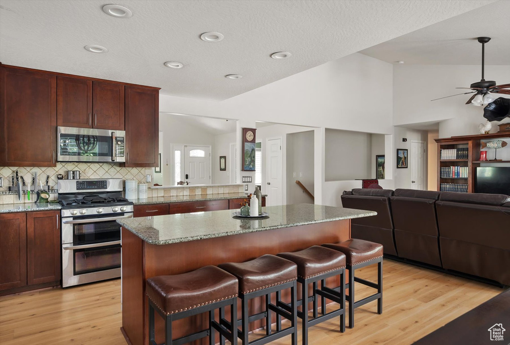 Kitchen featuring stainless steel appliances, decorative backsplash, light wood-style flooring, a kitchen island, and open floor plan