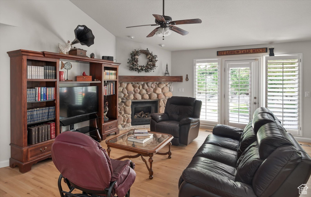 Living area featuring light wood finished floors, ceiling fan, and a stone fireplace