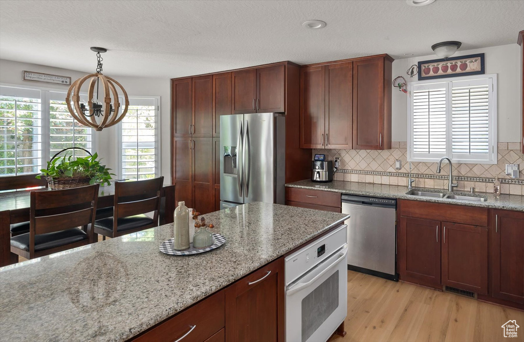 Kitchen featuring appliances with stainless steel finishes, a sink, a chandelier, light stone counters, and tasteful backsplash