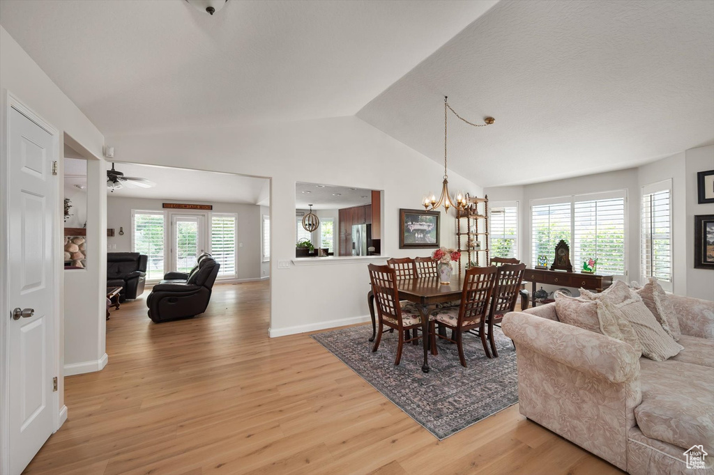 Dining area with light wood-type flooring, a chandelier, lofted ceiling, baseboards, and a ceiling fan