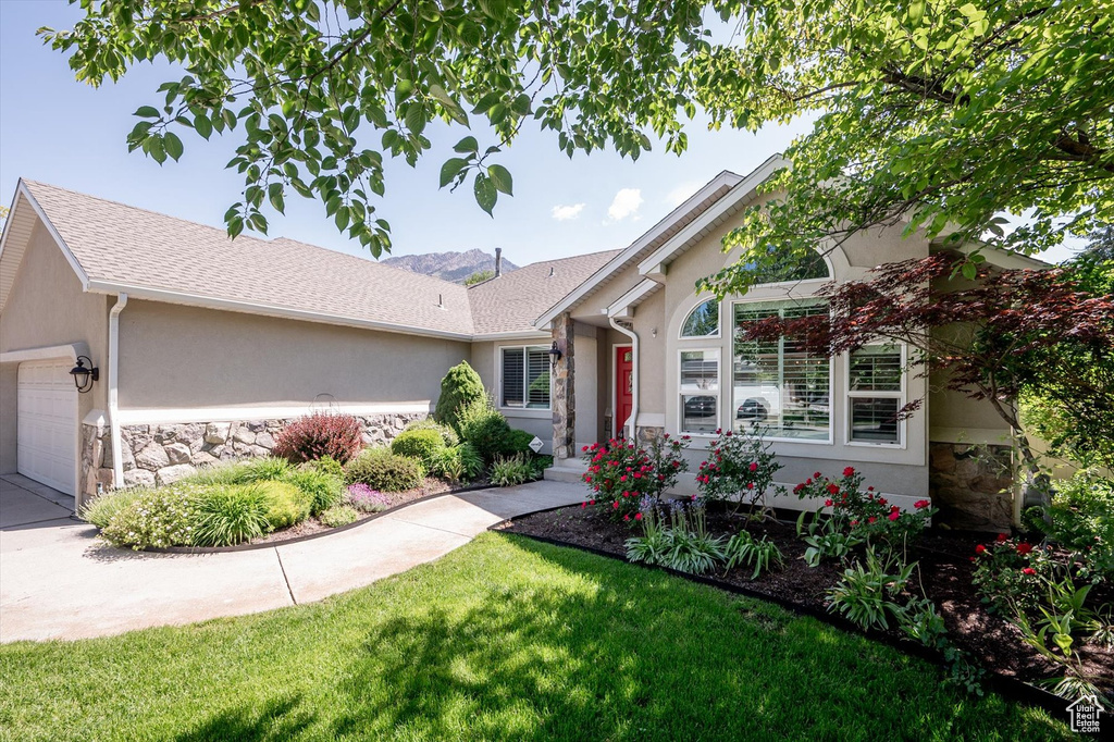 Ranch-style home with stucco siding, a garage, stone siding, and roof with shingles