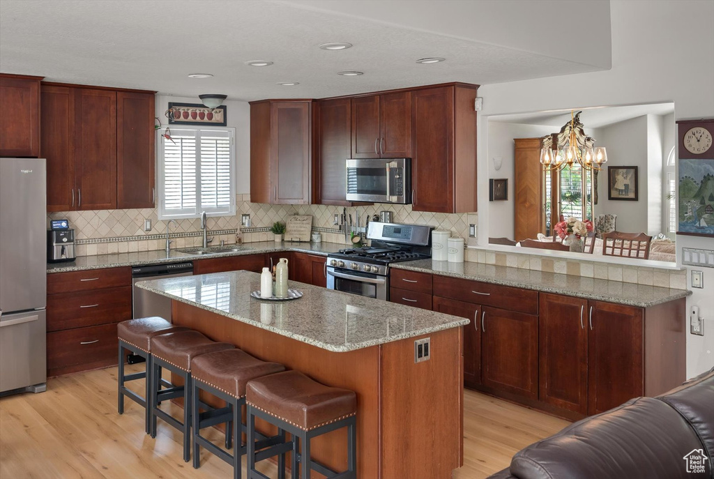 Kitchen featuring appliances with stainless steel finishes, a sink, light wood-style flooring, a kitchen breakfast bar, and a chandelier