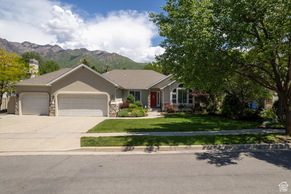 Ranch-style home with a garage, a mountain view, concrete driveway, a front lawn, and stone siding