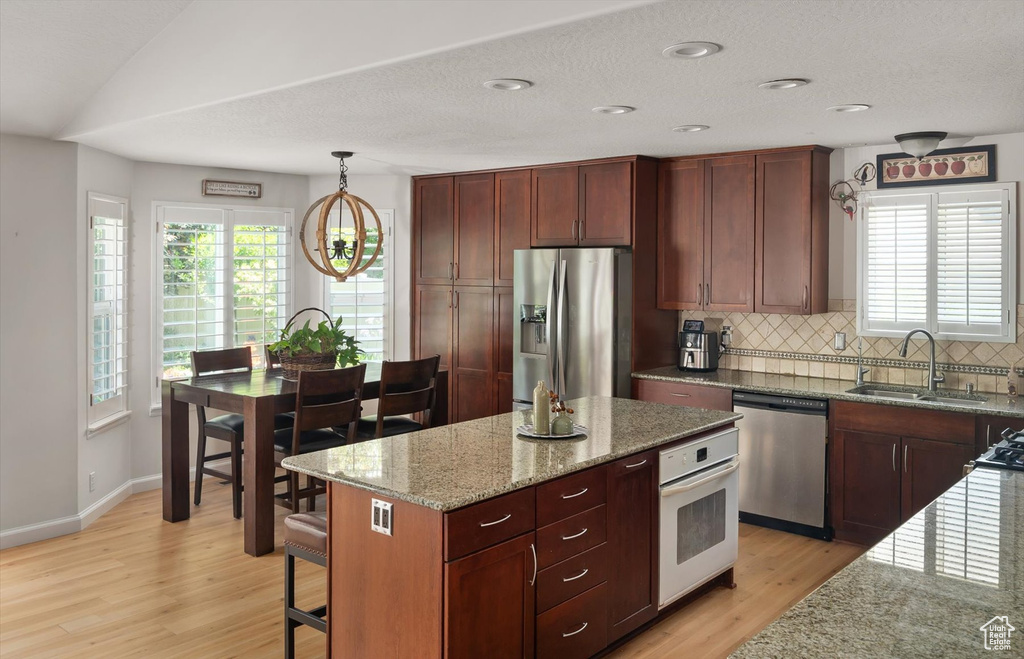 Kitchen featuring stainless steel appliances, light wood-type flooring, a sink, light stone countertops, and decorative backsplash