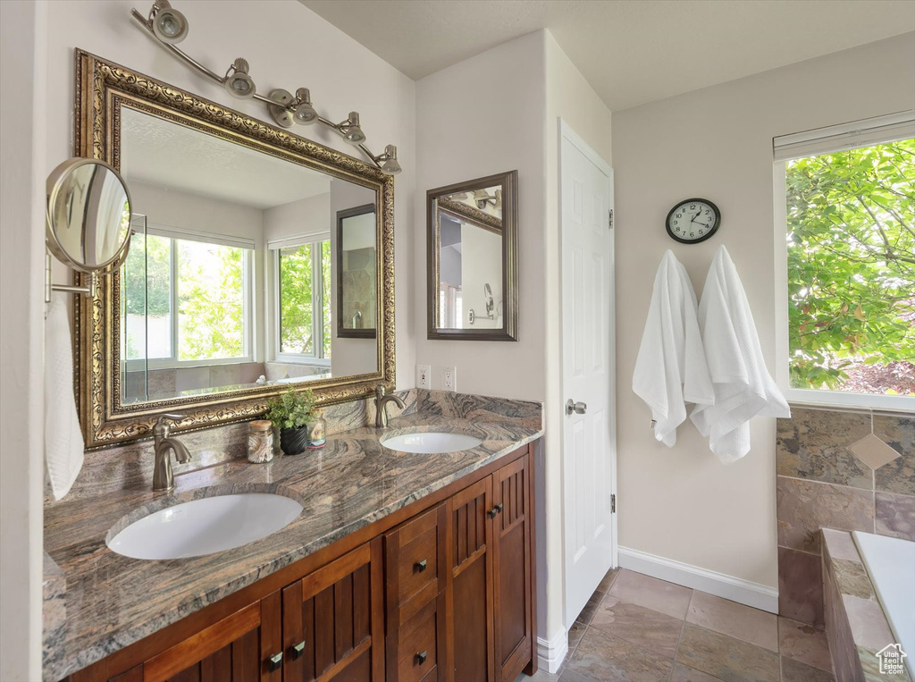 Bathroom featuring healthy amount of natural light, double vanity, baseboards, and a tub