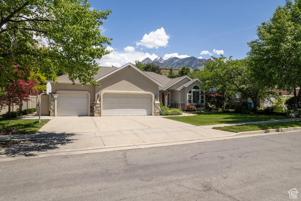 View of front of house with a garage, stucco siding, stone siding, a front lawn, and driveway