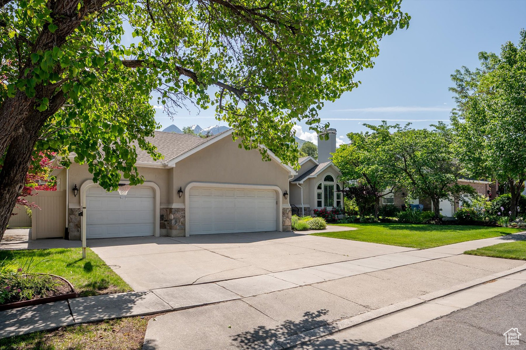 View of front of home featuring an attached garage, stone siding, a front yard, driveway, and stucco siding