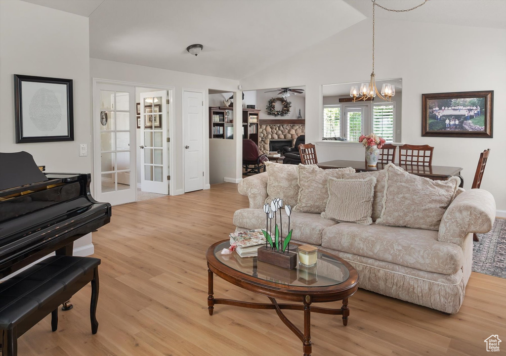 Living area featuring light wood-type flooring, a chandelier, a fireplace, lofted ceiling, and ceiling fan