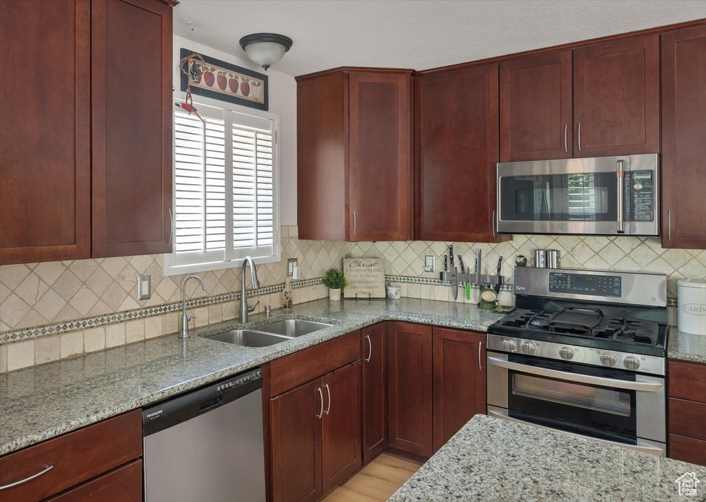Kitchen featuring appliances with stainless steel finishes, dark brown cabinets, a sink, and light stone counters