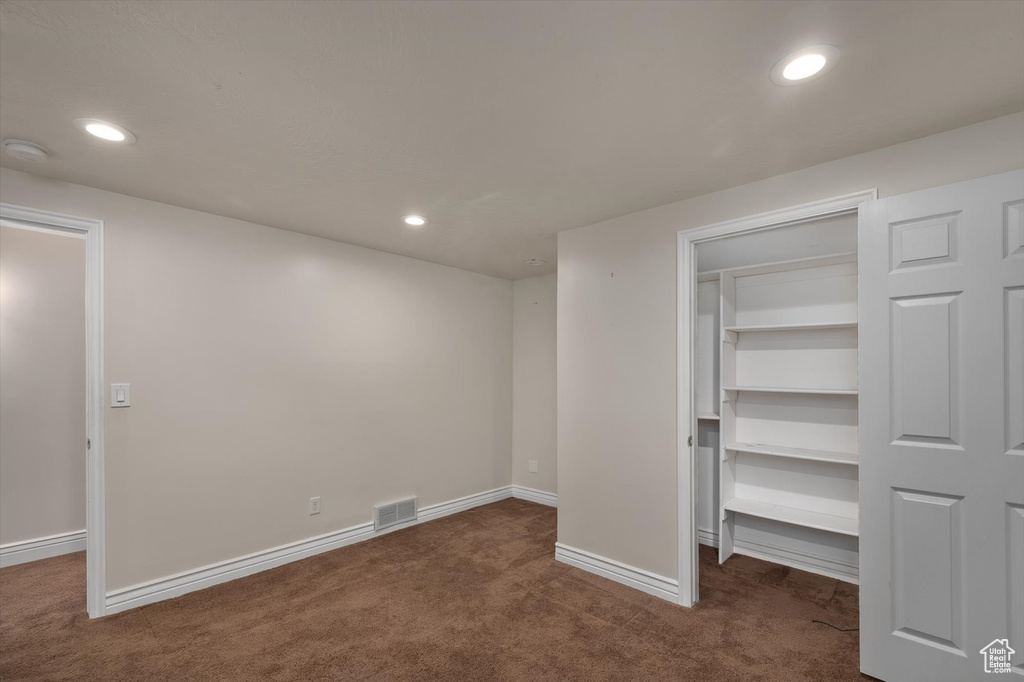 Unfurnished bedroom with dark carpet, a spacious closet, baseboards, recessed lighting, and a closet