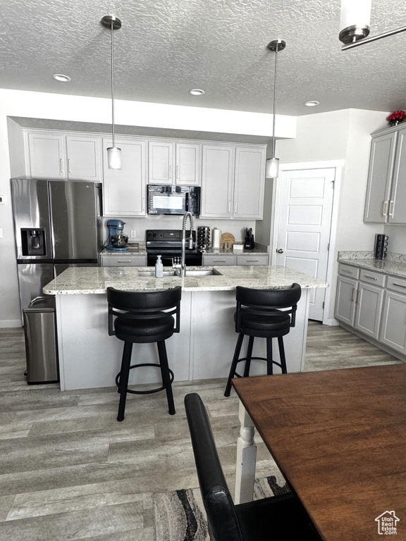 Kitchen featuring a sink, black appliances, light wood finished floors, a textured ceiling, and a kitchen breakfast bar