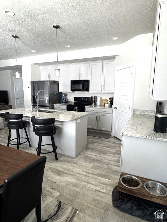 Kitchen with black appliances, a breakfast bar, a textured ceiling, an island with sink, and light stone counters