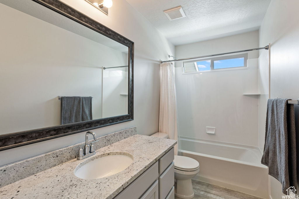 Bathroom with wood finished floors, shower / bath combination with curtain, vanity, toilet, and a textured ceiling