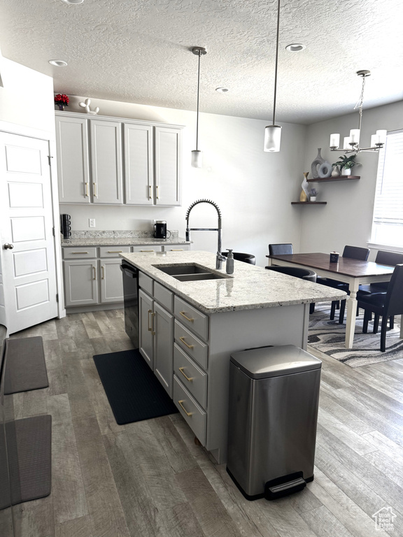 Kitchen featuring a sink, wood finished floors, dishwasher, a textured ceiling, and gray cabinetry
