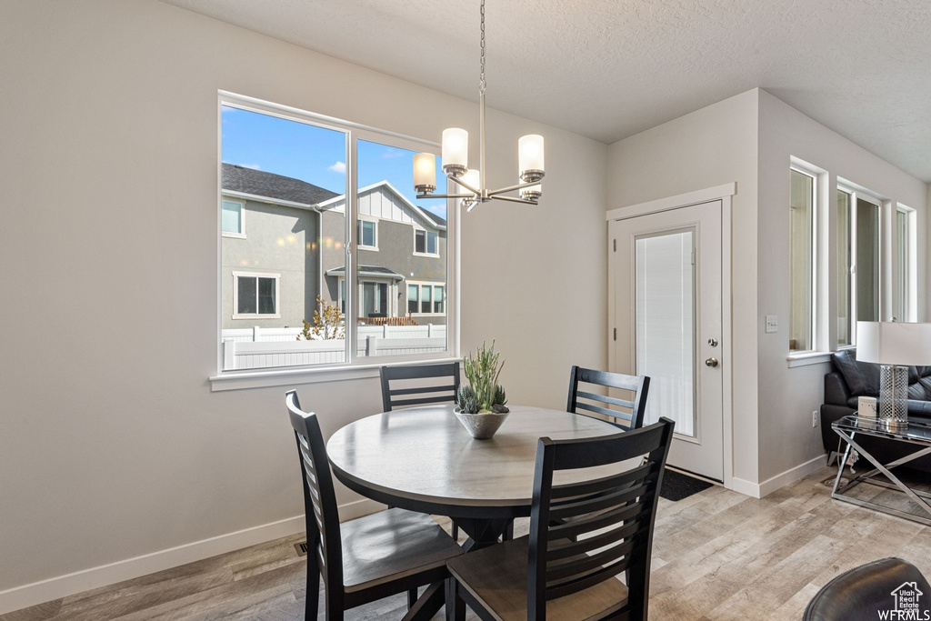 Dining space with light wood finished floors, baseboards, a chandelier, and a textured ceiling
