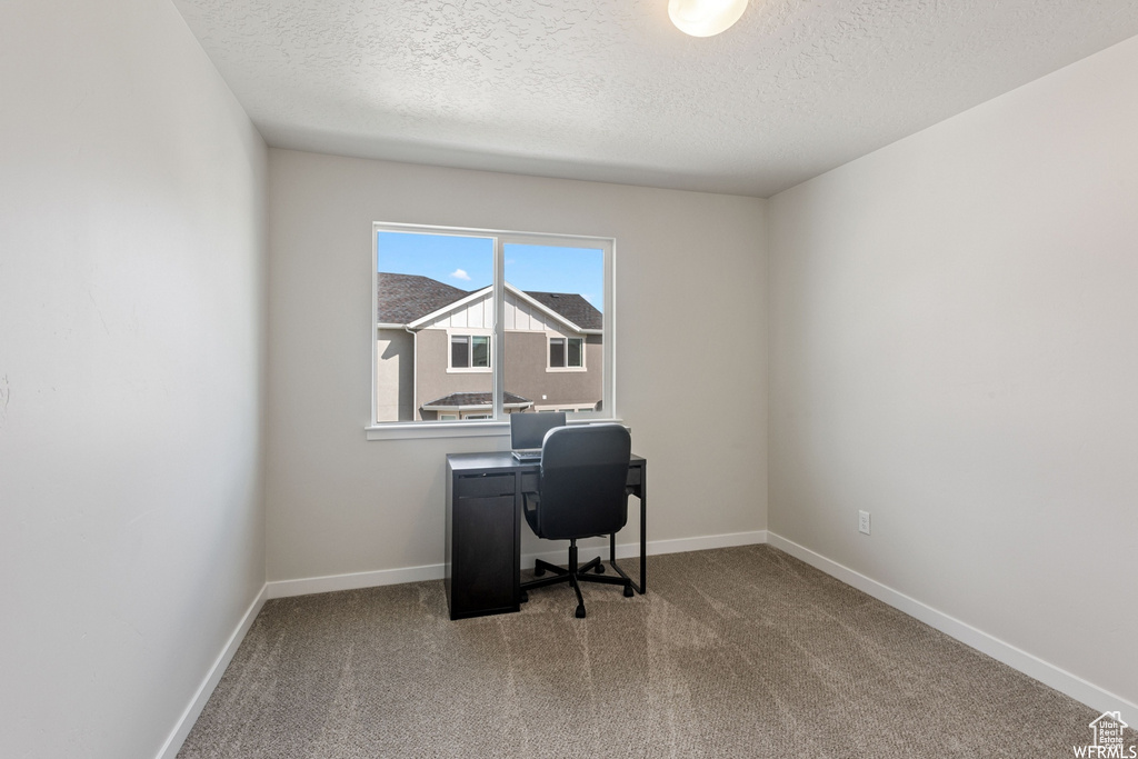 Carpeted home office featuring a textured ceiling and baseboards