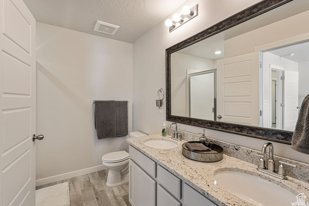 Bathroom with wood finished floors, a stall shower, toilet, baseboards, and double vanity