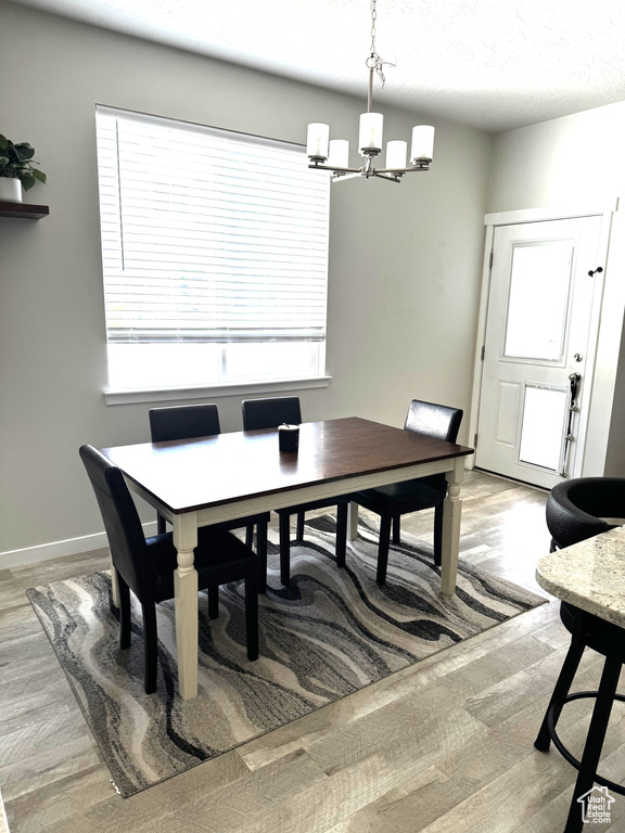 Dining space featuring a chandelier, light wood finished floors, baseboards, and a textured ceiling