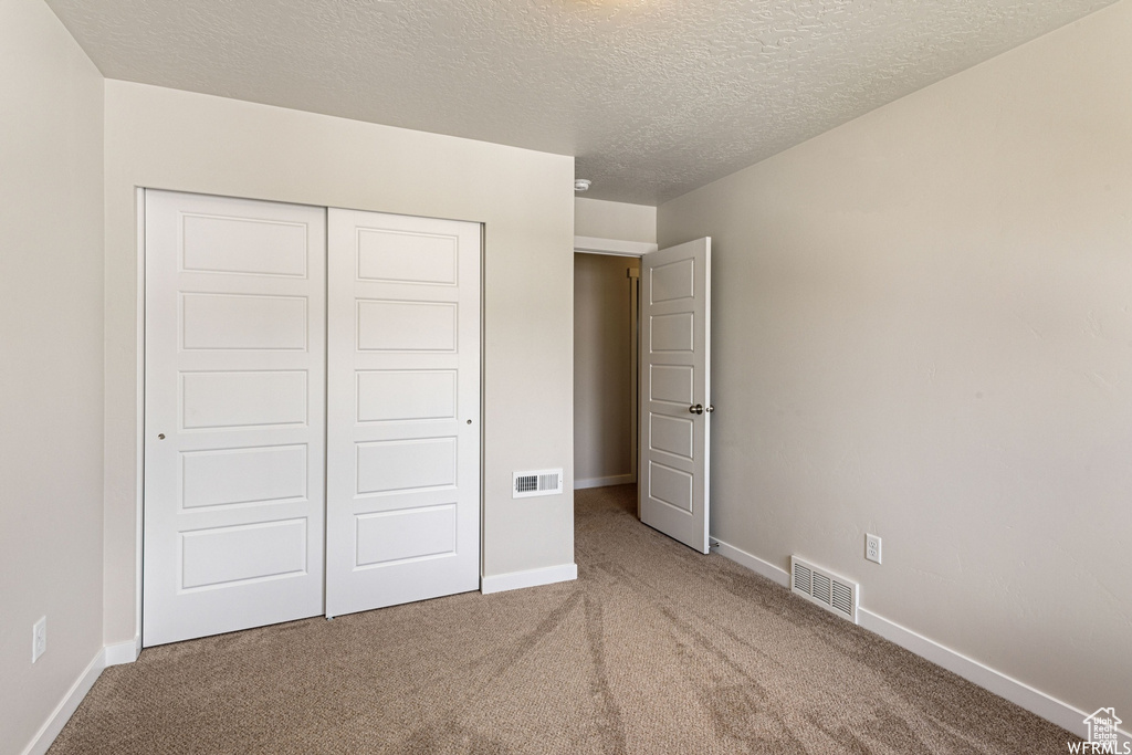 Unfurnished bedroom featuring carpet flooring, a closet, a textured ceiling, and baseboards