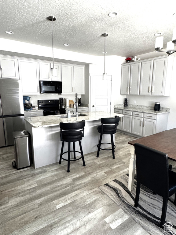 Kitchen featuring black appliances, light wood finished floors, a kitchen breakfast bar, a textured ceiling, and an island with sink