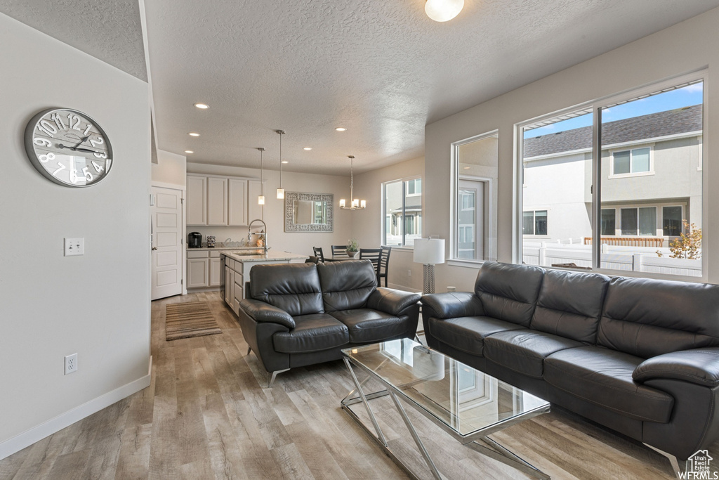 Living room with a textured ceiling, light wood-style flooring, baseboards, a chandelier, and recessed lighting