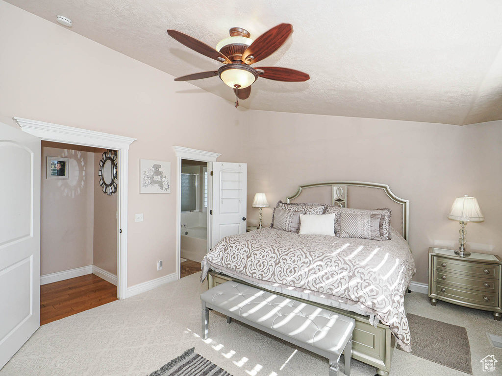 Carpeted bedroom with vaulted ceiling, a textured ceiling, baseboards, ceiling fan, and connected bathroom