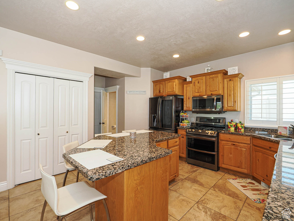 Kitchen featuring stainless steel appliances, a sink, a center island, a kitchen bar, and brown cabinets
