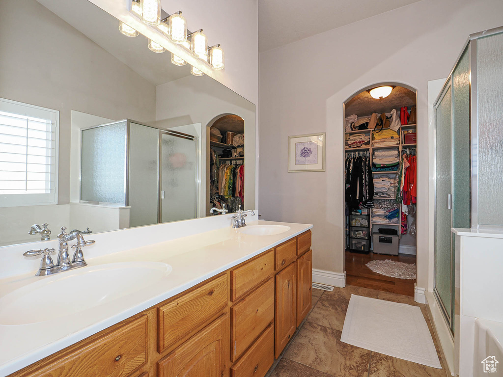 Full bath featuring a shower stall, double vanity, and baseboards