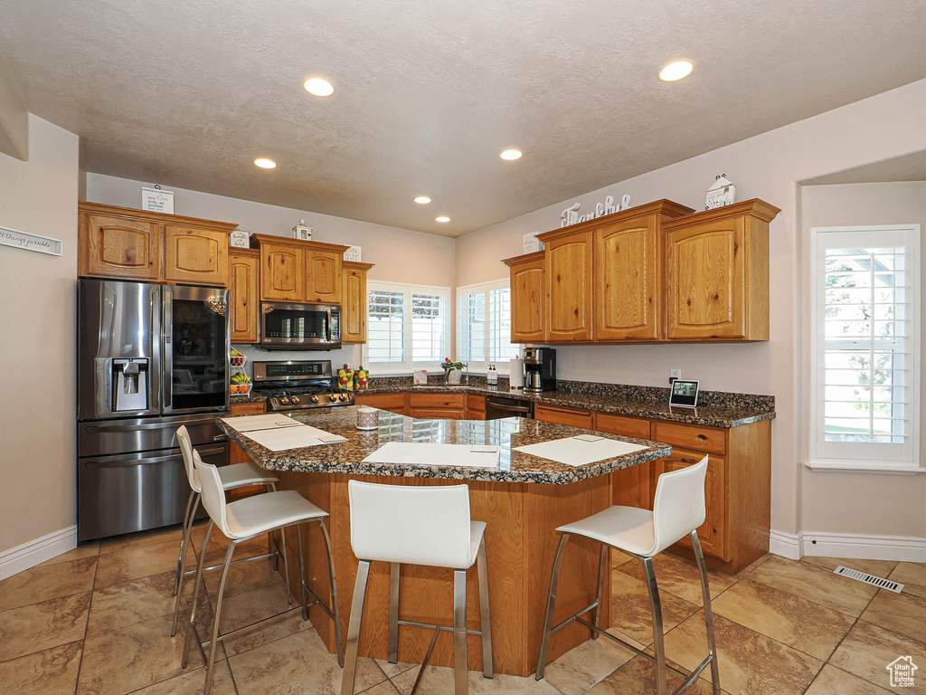 Kitchen with appliances with stainless steel finishes, a center island, baseboards, a breakfast bar, and recessed lighting