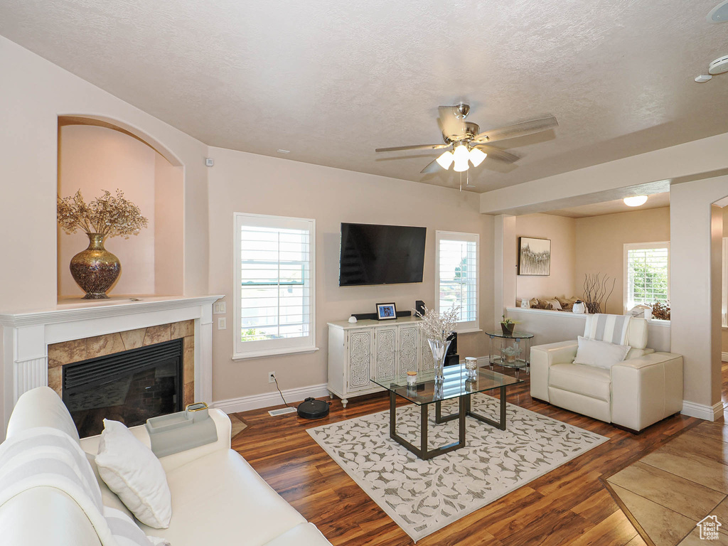 Living room with ceiling fan, a fireplace, wood finished floors, baseboards, and a textured ceiling